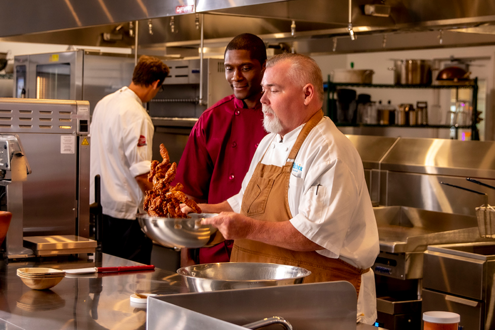 Chef tossing chicken in a sauce in the kitchen